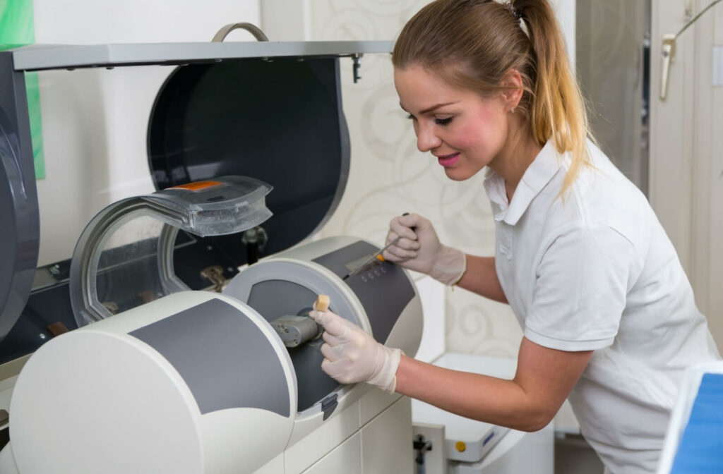 A female dental assistant operating a CEREC Milling machine to produce dental crowns.