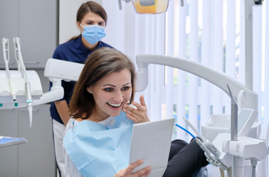 A woman at the dental clinic is holding a mirror with a happy face being happy on her newly installed dental dental implant
