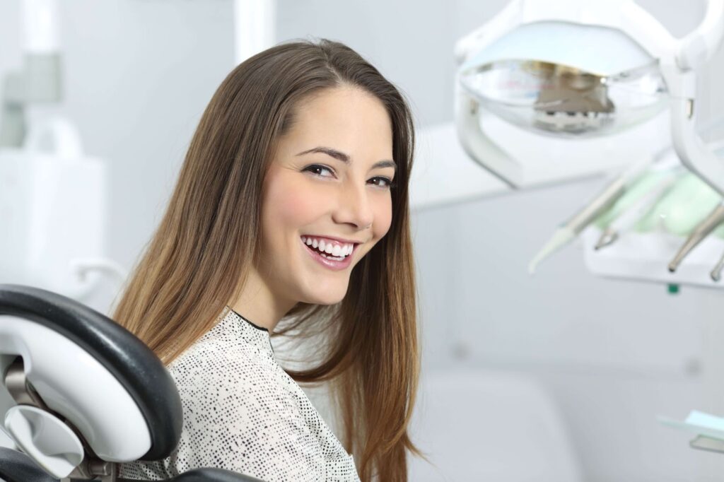 a woman sitting in a dentist chair turns around while smiling