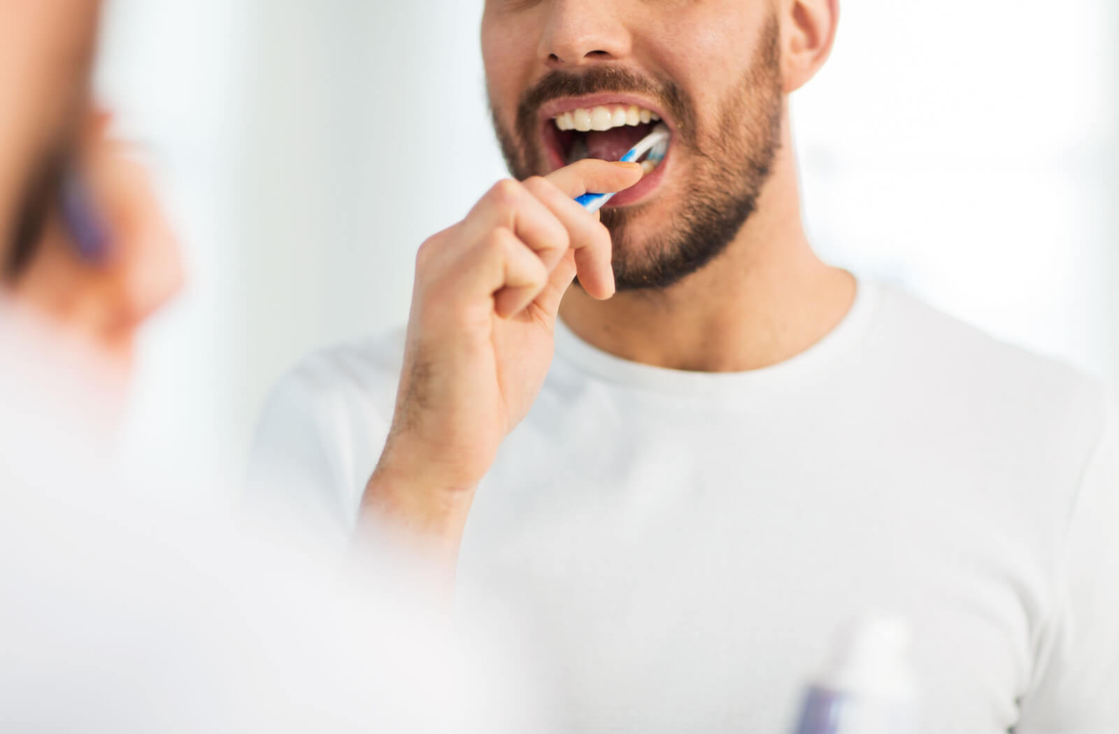 smiling man in a white shirt brushing his teeth