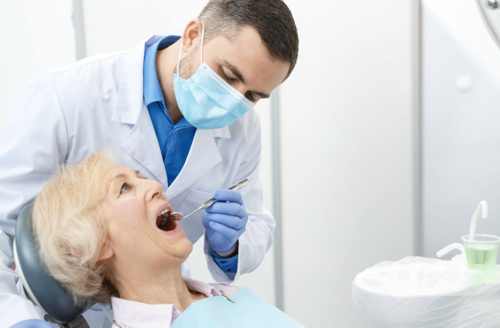 a senior woman has her mouth examined by a dentist with a hand mirror